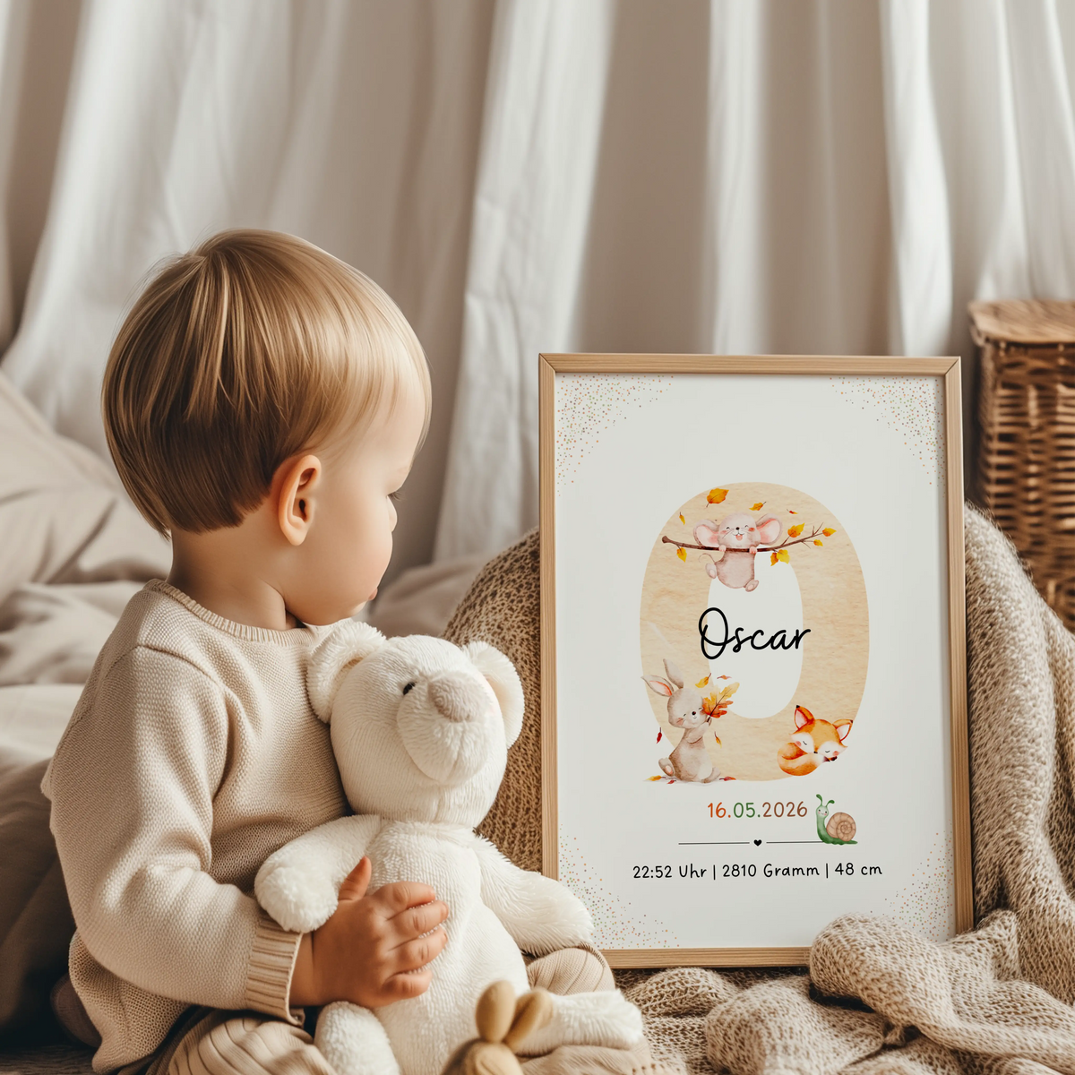 Baby sitzt mit Plüschelefant und schaut auf ein personalisiertes Buchstabenposter Herbst mit Waldtieren.